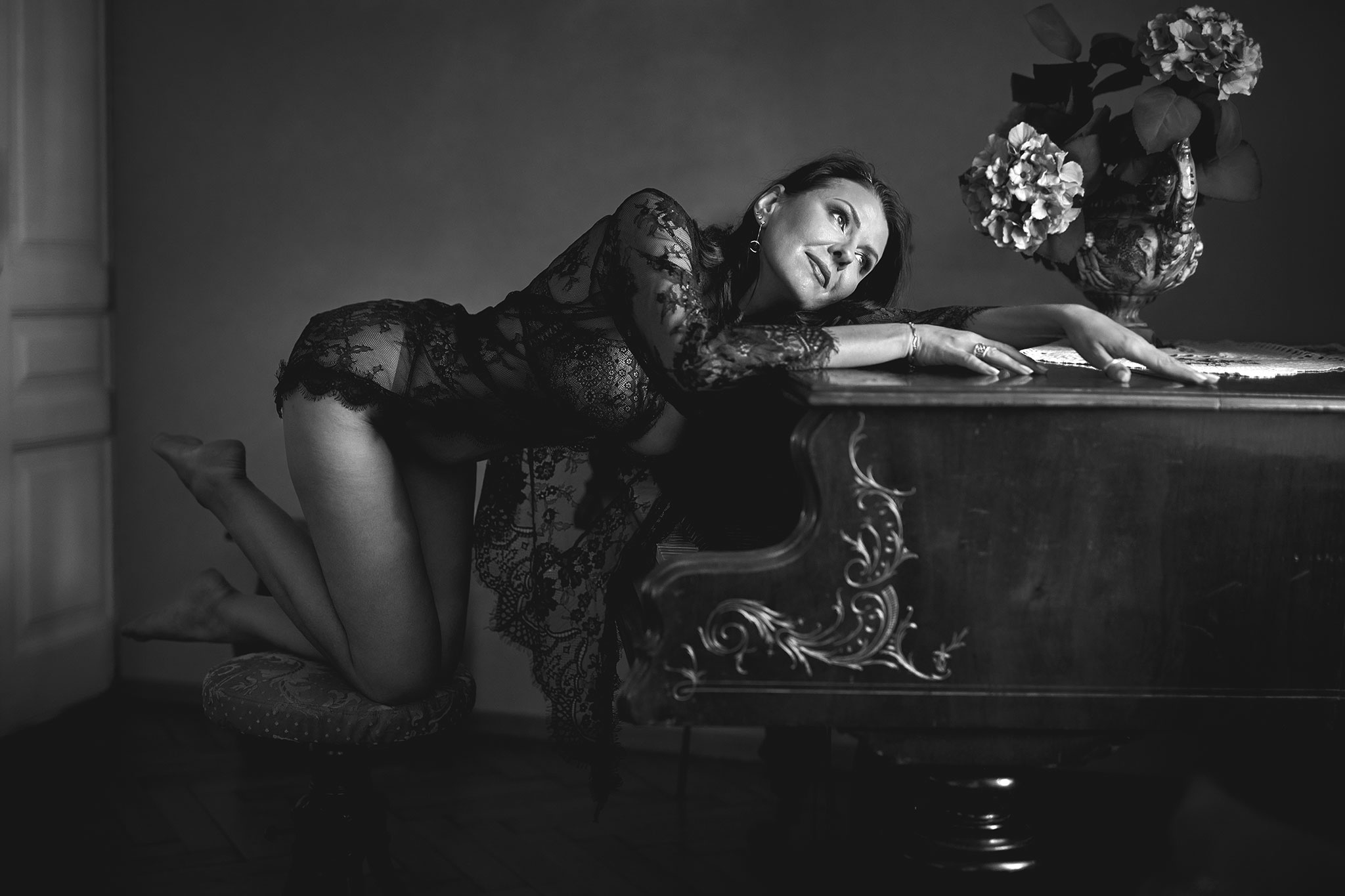 En mørkhåret kvinne i morgenkåpe kneler på en krakk og ligger på pianoet